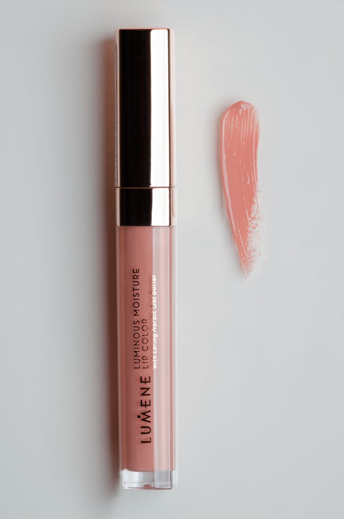 Flat lay of pink lip gloss with applicator swipe on white background.
